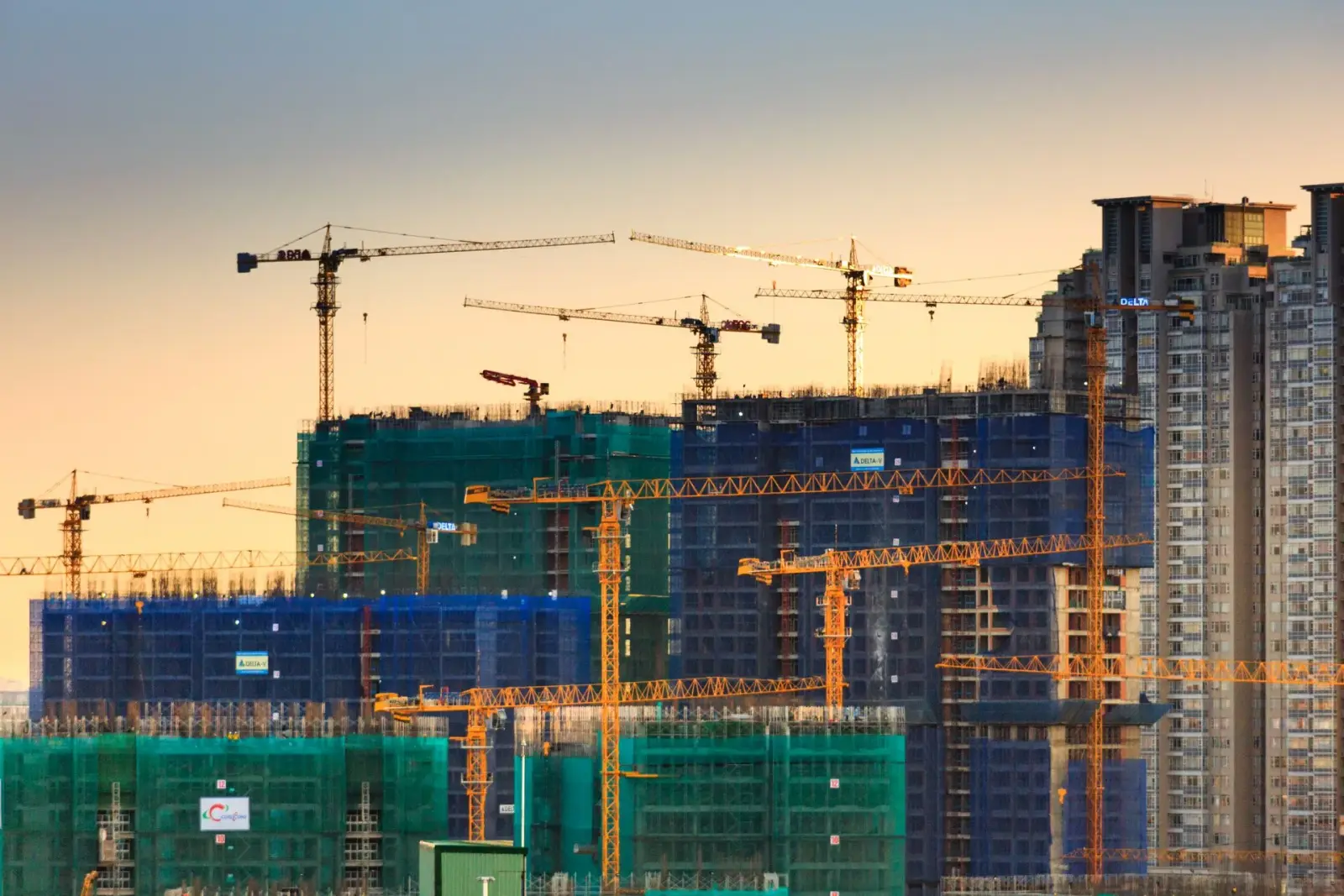 Tower cranes above buildings under construction in warm evening light